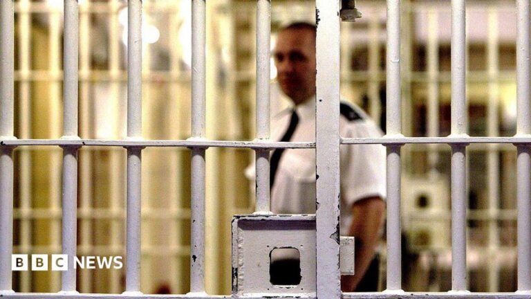A prison guard at HMP Pentonville stands behind a locked gate