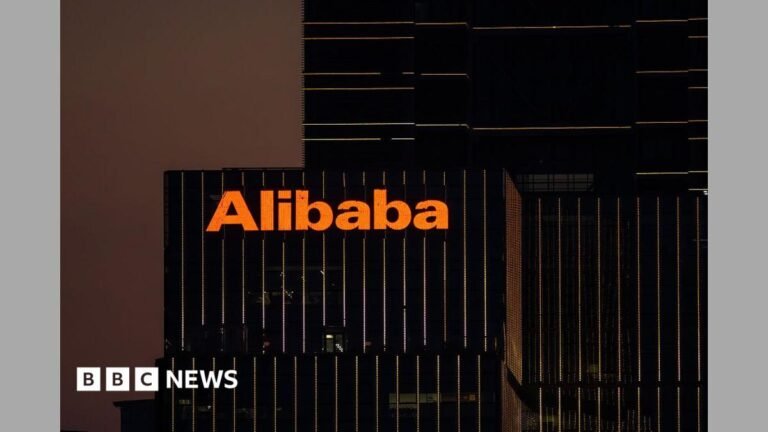The Alibaba logo in orange lights is displayed on the exterior of an office that appears with black windows at dusk.