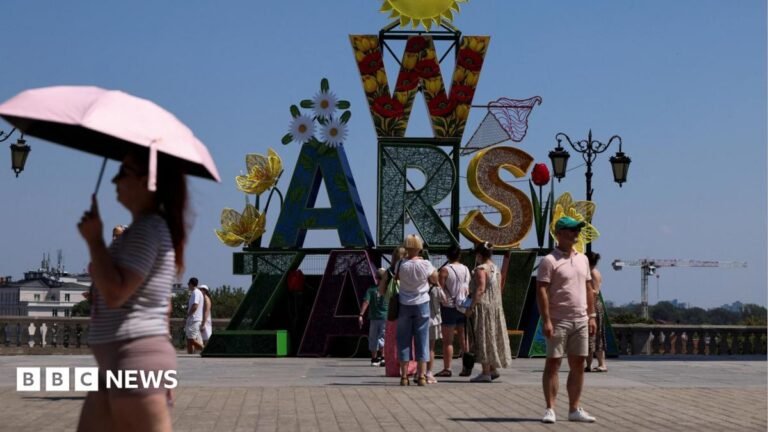 A woman walks under an umbrella past a "Warsaw" sign as a heatwave sweeps Poland, in Warsaw, Poland,