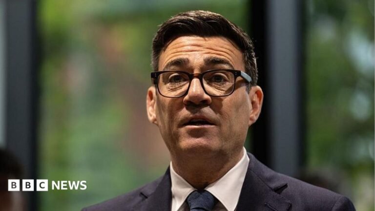 Andy Burnham to address social care, youth unemployment and devolution A picture of Andy Burnham from the shoulders up. He is wearing a dark suit with a white shirt and dark tie, has thick-rimmed black glasses on, and has short, dark brown hair. The background behind him is blurred and he is looking forward with his mouth slightly open and his eyebrows raised.
