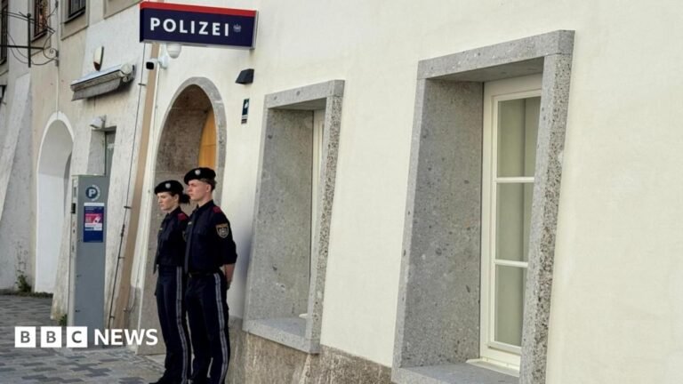 Two police officers stand outside a white-washed building with a police sign in German on the wall