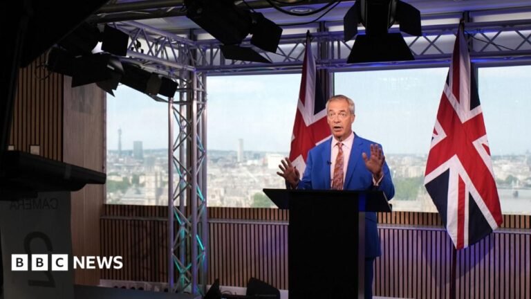 Nigel Farage in a blue suit and pink shirt and tie, standing in front of a blue background with a union flag in the background