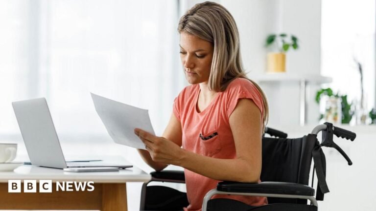 Disability benefit not fit for purpose, minister leading review says A woman sitting in a wheelchair in front of her laptop, looking at paperwork.