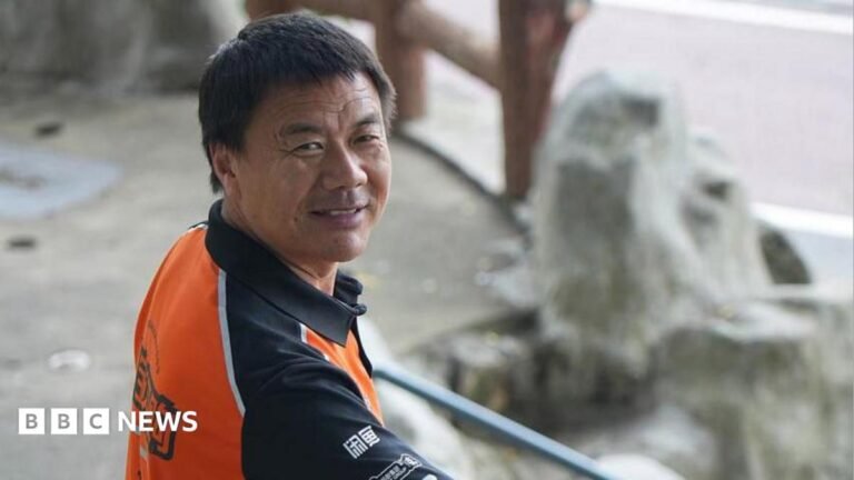 Wang Jibing in an orange polo shirt smiling at the camera