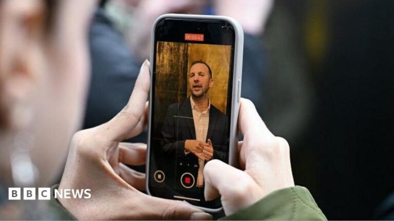 Greens review social media operation as Polanski row rumbles on Two hands holding a phone with Zack Polanski on the screen