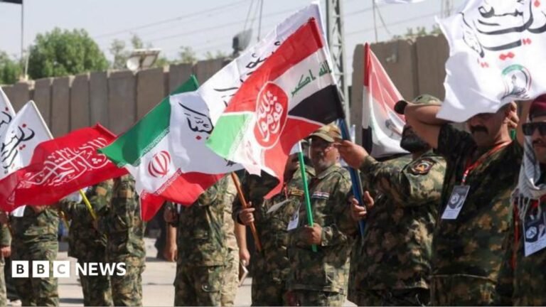 Iran targets military bases as US launches wave of strikes Iranian military personnel stand in a line waving red, white, green and black flags.