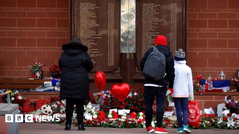 MPs expected to approve long-delayed ‘Hillsborough Law’ People stand in front of the Hillsborough Memorial outside Anfield Stadium in Liverpool. There are flowers and heart balloons in front of a plaque with the names of the victims of the disaster.