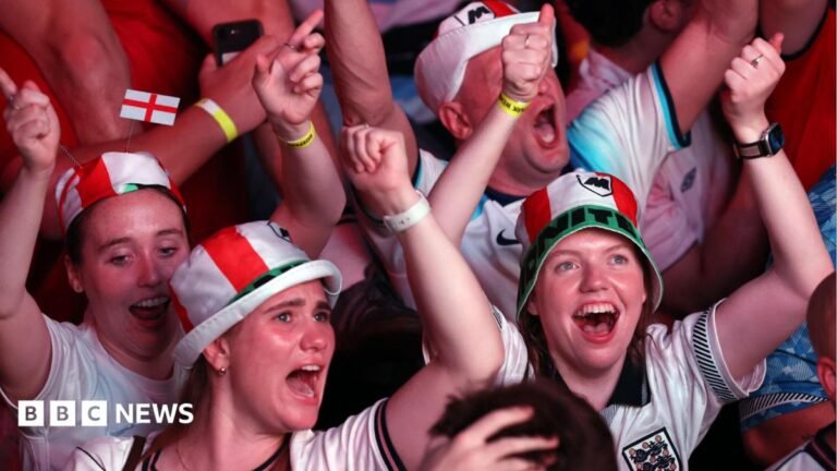England fans dressed in red and white hats celebrate with their arms raised during a World Cup match.