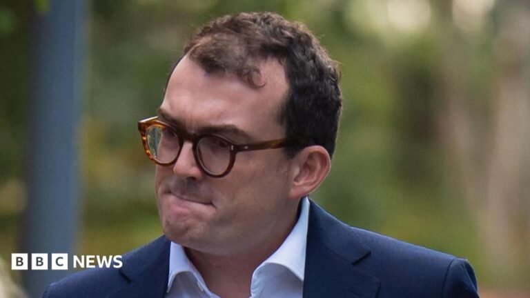 Suffolk MP Patrick Spencer arrives at court for sexual assault trial A man who has short dark hair, glasses and who is wearing a navy suit jacket and white shirt. He is looking away from the camera.