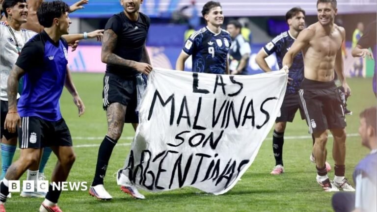 Argentina players hold a white banner that has "Las Malvinas son Argentinas", which translates as "The Falklands are Argentine", written in black text.