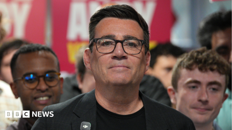 Union backing to seal Labour leadership for Andy Burnham Catherine Turnbull is smiling at the camera. She is wearing a pale blue t-shirt and dark framed glasses. Catherine has short light brown hair. She has some bushes behind her with are slightly out of focus.