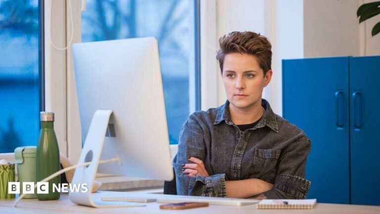 Virtual interviews don’t show bosses your personality, says Burnham A young woman with short hair wearing a grey denim shirt working in an office, sitting with arms crossed at the desk in front on computer.