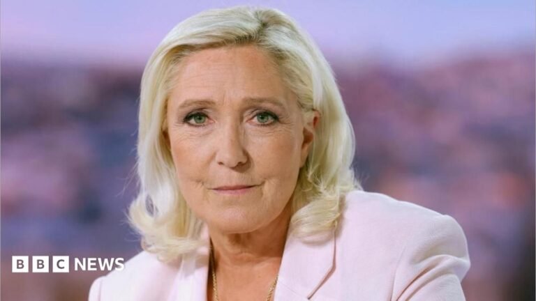 Le Pen raises a finger while looking back at a man with a dark suit and tie and a white shirt