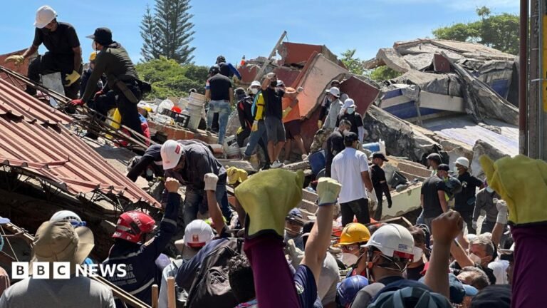 Anguish of Colombian brother at rubble of building being searched for earthquake survivors Alejandro Mahecha, he's a young person wearing a blue hard hat and a black t-shirt - he has medium length hair and has a serious expression
