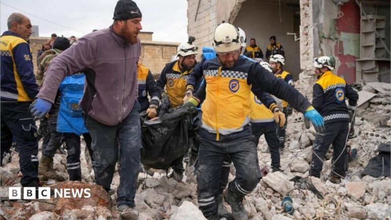 Rescuers carry a body bag across rubble