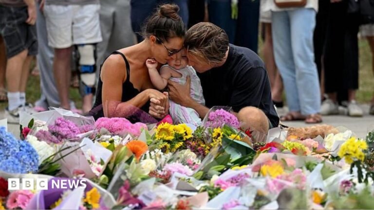 Australian state to begin gun buyback after Bondi Beach attack A woman with dark hair wearing a black strappy top and a man with dark blonde hair wearing a black shirt hug a young child as they kneel at a floral tribute to the Bondi Beach shooting victims at the Bondi Pavillion in Sydney on 15 December, 2025.
