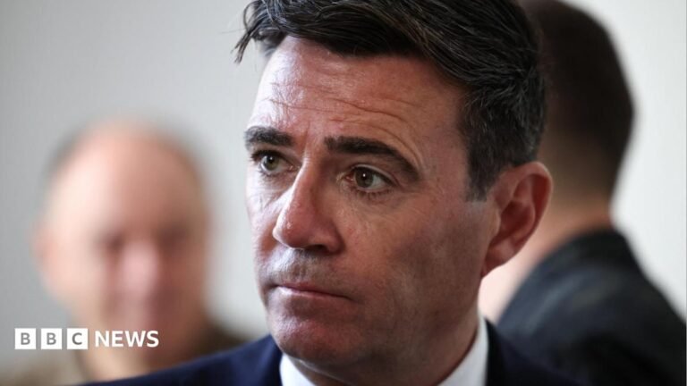 Andy Burnham wearing a black suit and white shirt, looking to the left of the frame of the photograph. The picture is a close up with most of Burnham out of shot bar his head and shoulders.