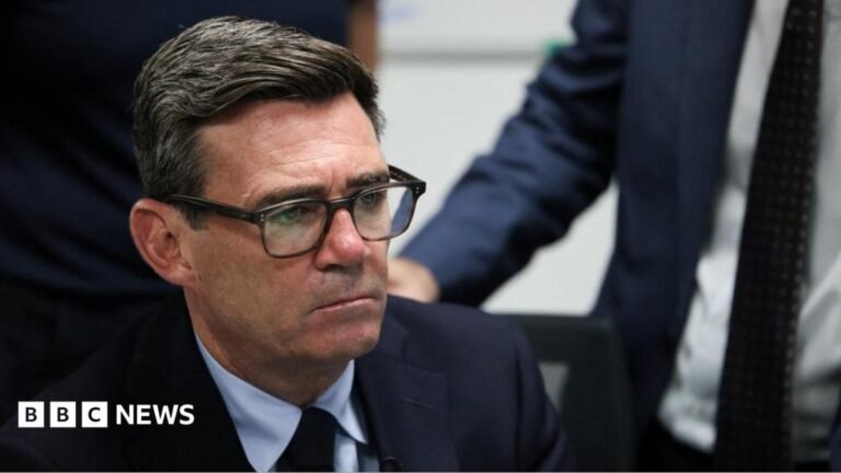 Prime Minister Andy Burnham talking while adjusting his glasses