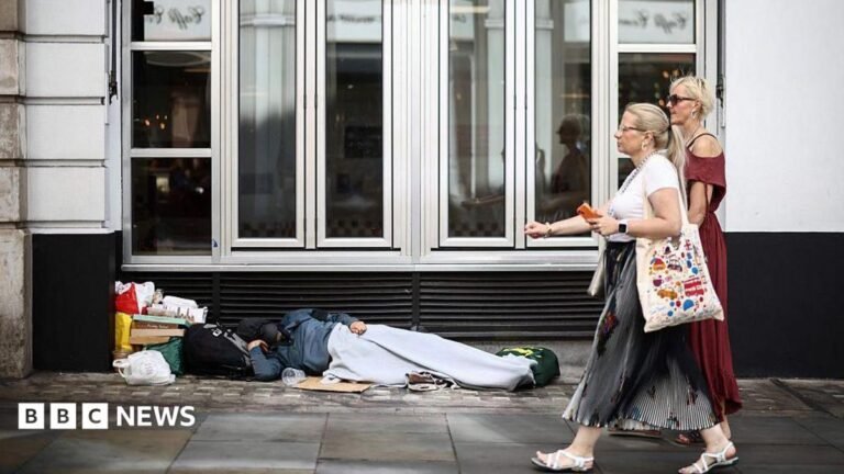 ‘Everyone in for Christmas’ – Burnham’s rough sleeping plan Two women walk past a person lying on the pavement in London, 28 July