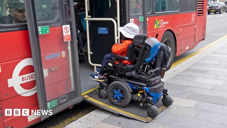 Free bus travel for disabled people in England to be extended to 24 hours a day A person in a motorised wheelchair wearing an orange jacket and a white hat boards a bus in London using a wheelchair ramp in October 2025