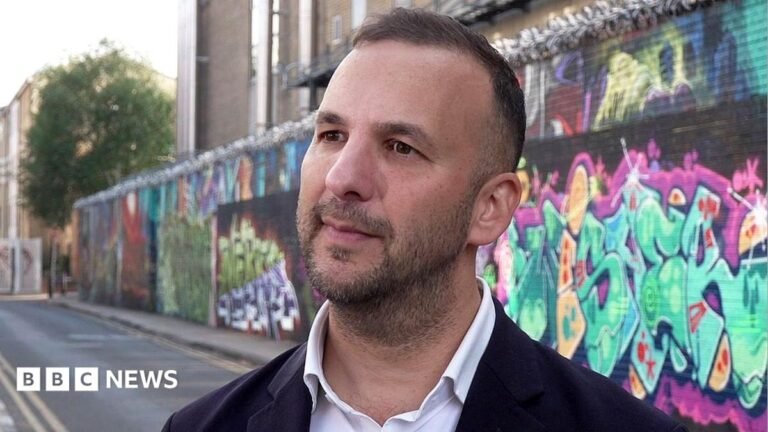 Greens call for temporary ban on new data centres Zack Polanski, an unshaven man with a short haircut, in an open neck shirt is standing in a street against a backdrop of a wall covered in graffiti