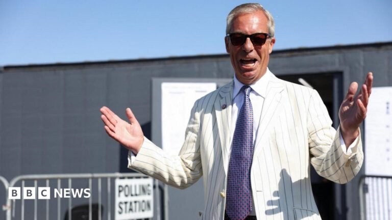 Has Farage’s by-election win changed things for Clacton? Nigel Farage standing outside a polling station, in a grey portable building, with his hands outstretched and raised. He is wearing a white jacket with blue pinstripes on it, a patterned lilac tie and sunglasses.