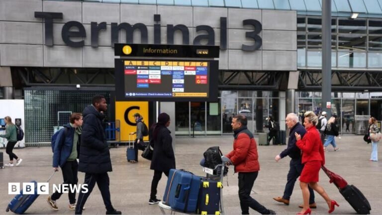 Passengers push luggage outside Terminal 3 as a gate information screen can be seen in the background