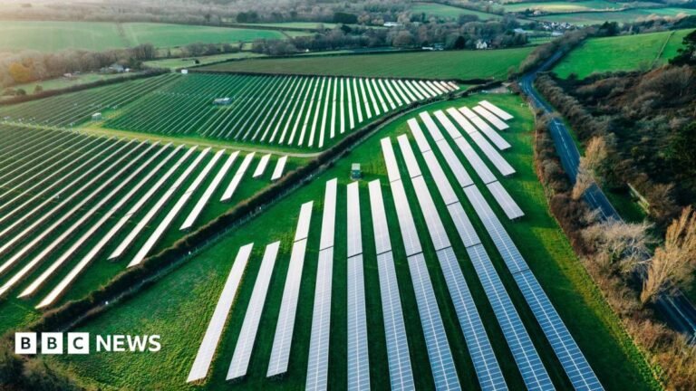 A stock picture of a solar farm. There are rows of solar panels in a field.