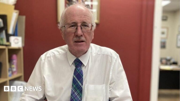 Jim Shannon: DUP MP charged with common assault of a woman Jim Shannon, a man with grey hair and glasses, wearing a white shirt and blue tie.