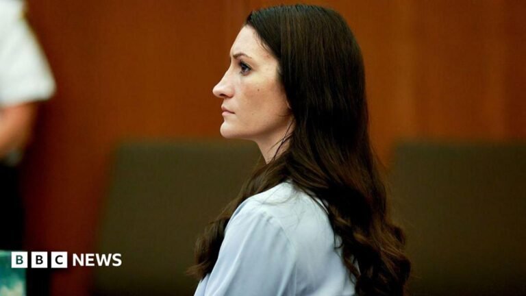 Lindsay Clancy begged for help before her children’s killings, mother-in-law testifies Lindsay Clancy in court. Long brown hair hangs down her back as she sits wearing a pale blue shirt.