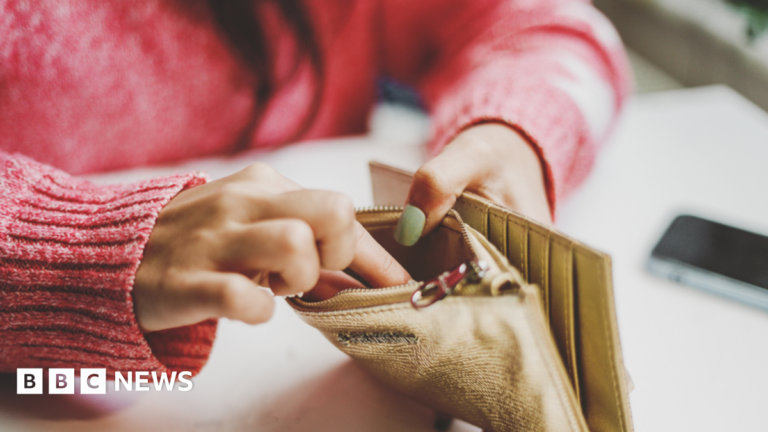 Person with red jumper has fingers inside gold coloured wallet.