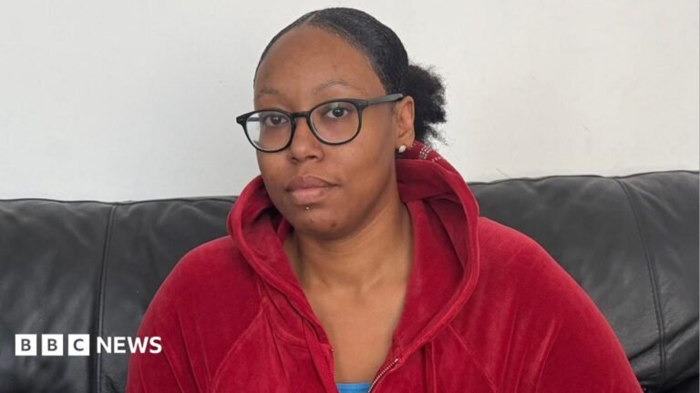 Number of children in temporary accommodation hits record high Ronesha is wearing a red hooded top and sitting on a black sofa with a painted wall behind her.