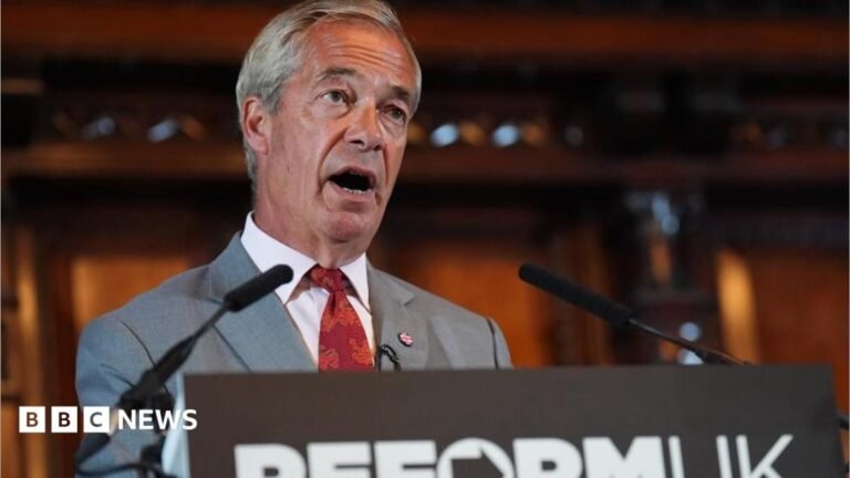 Ofcom investigating Sky News over Farage harassment claims Nigel Farage, wearing a grey suit with a Union Jack pin on his lapel, and a red tie is speaking in front of a lecturn with a Reform UK logo on the front. The background is blurred.