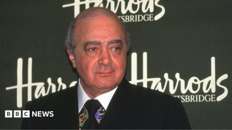 The late former Harrods owner Mohamed Al-Fayed standing in front of the Harrods logo