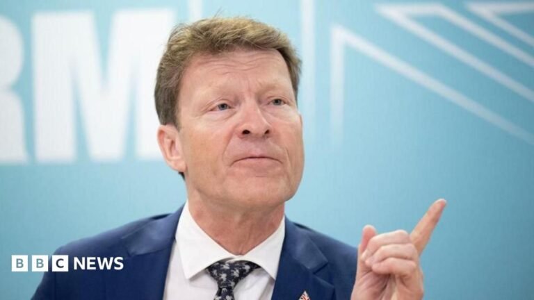 Reform says it will prioritise British-born young workers for social housing Richard Tice, in blue jacket, white shirt, and black and white tie, points with his finger while talking to reporters