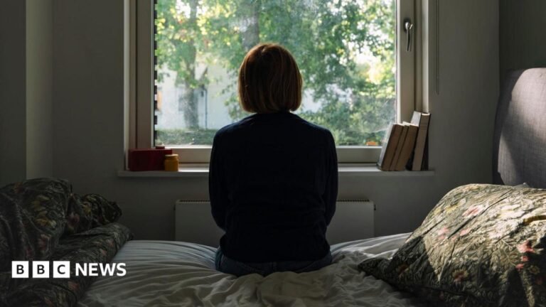 Restriction zone scheme for offenders to start in October A woman looks out of a window while sitting on a bed.