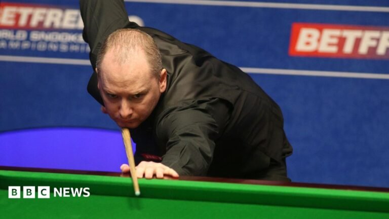 A balding man in a black shirt holds a snooker cue as he prepares to take a shot