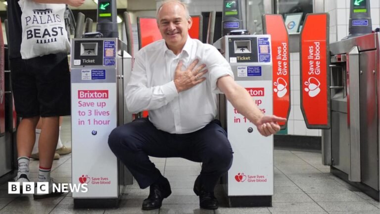 South of France holiday scuppers Ed Davey’s blood donation Ed Davey crouches in front of tube barriers, which are advertising the nearby blood donation centre. The adverts read: "Brixton: Save up to 3 lives in 1 hour." Ed Davey is wearing dark trousers and a white shirt with one sleeve rolled up as if about to donate blood.