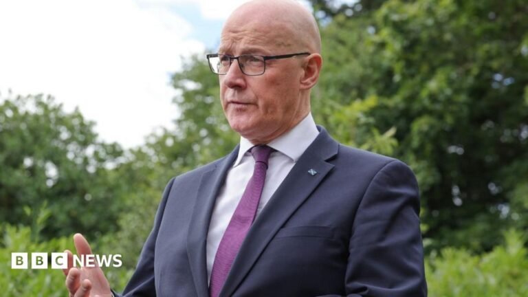 Swinney calls for Burnham rethink on Chinese factory in Highlands John Swinney, who is bald with glasses, speaks outdoors with leafy green trees in the background. He is wearing a business suit.