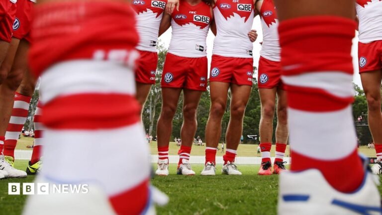 Sydney Swans: Aussie rules players referred to police as detectives investigate sexual assault A pair of blurry legs in the foreground with a line of Sydney Swans players in the background