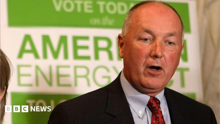 Thousands of Canadians call for US ambassador’s expulsion Pete Hoekstra, with short grey hair, and in a dark suit coat, red tie and patterned blue shirt, stands in from of a green and white campaign sign promoting American energy.