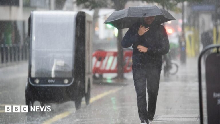 Yellow thunderstorm warnings issued for parts of UK by Met Office A man wearing a sodden jacket and trousers carries an umbrella down a street through a downpour