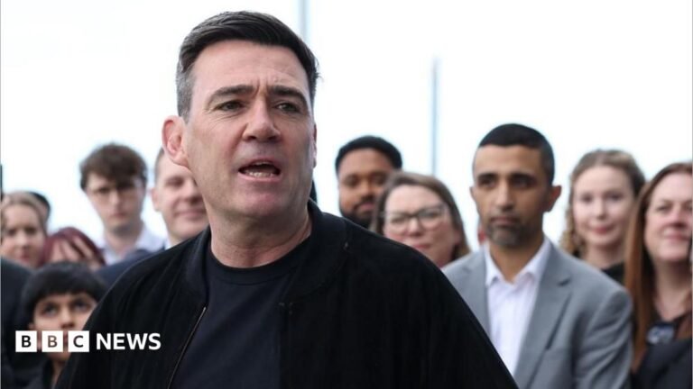 Andy Burnham announces scheme to help first-time buyers Andy Burnham is wearing a dark jacket over a dark top. He is stood in front of a crowd of people and is speaking.
