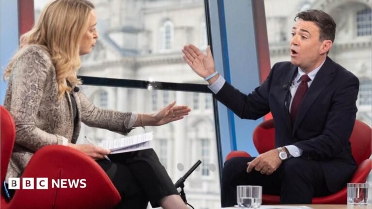 Andy Burnham proposes NHS-style social care system for England Laura Kuenssberg is sat on the left and Andy Burnham is sat on the right. They are sat in red chairs. Kuenssberg is wearing a grey jacket and black trousers. She is holding sheets of paper and a pen. Burnham is wearing a dark coloured suit and red tie.