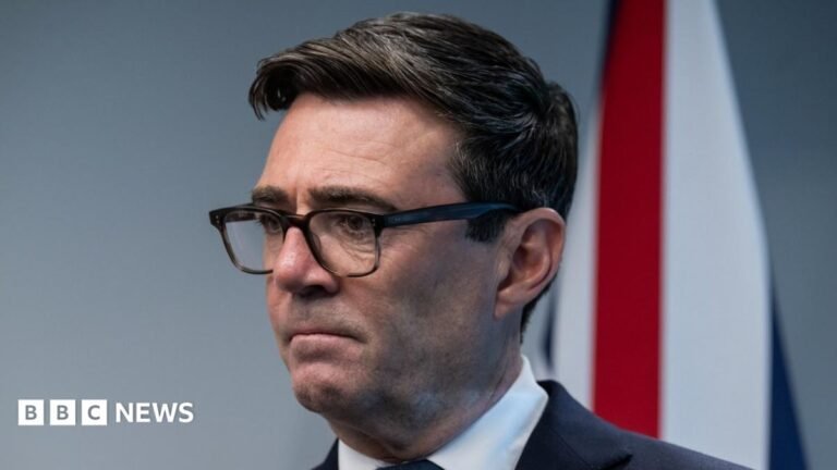 Andy Burnham urged to set dementia waiting-time target Alex Batty has short brown hair and is wearing glasses, and an orange high vis jacket.