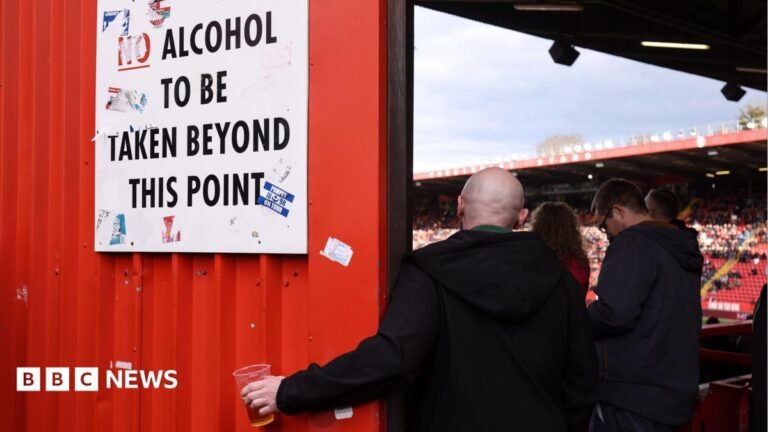 Burnham brands ban on football fans drinking alcohol in stands as ‘discrimination’ A football fan holds his pint of beer beneath a sign instructing that no alcohol should be taken beyond this point so he can continue to watch the match. The fan has his back to the camera and is wearing a dark-coloured jacket.