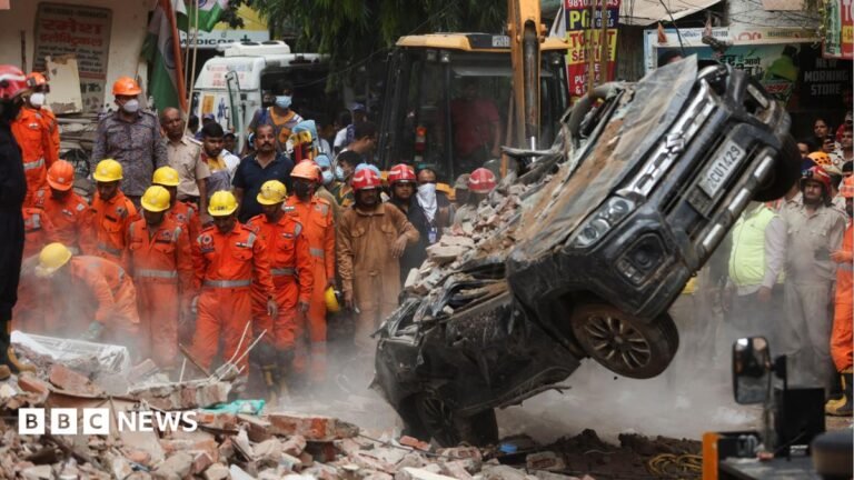 Dozens feared trapped in collapsed building in Delhi National Disaster Response Force (NDRF) personnel look on at a building collapse in Delhi, while a crushed car is pulled by a digger from the rubble.