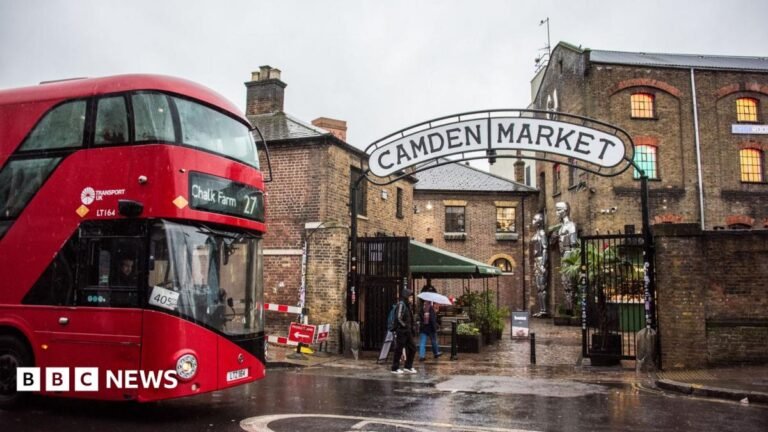 A red London bus heading to Camden Town passes by the entrance to Camden Market.