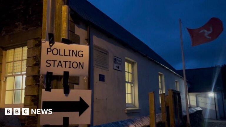 A sign reads polling station with an arrow, there is a Manx flag flying in the background.