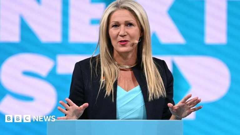 Laura Anne Jones stood at a podium in front of the words "Next Step" in Reform fontsetting and teal colours.